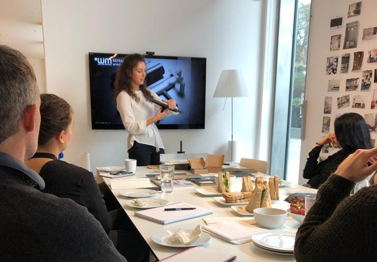 Woman giving a presentation in front of an audience with a screen displaying a logo.