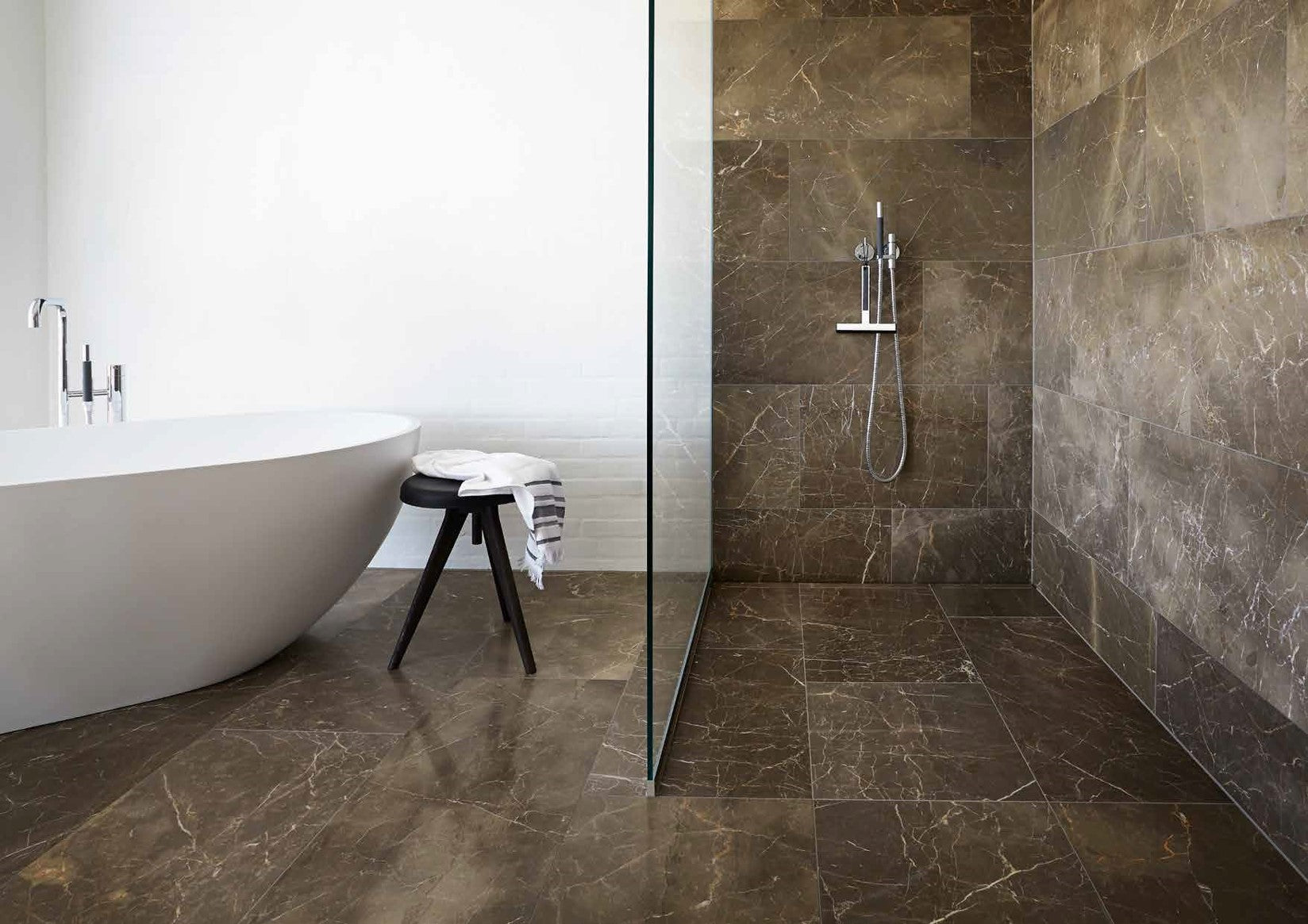 Modern bathroom with a freestanding bathtub, stool, and shower area.