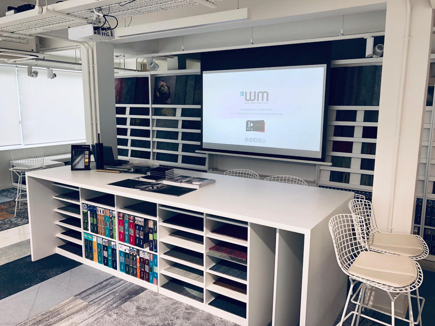 Modern office space with a large desk, chairs, and a screen displaying a logo.


